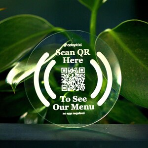 May include: A clear round sticker with a white QR code and the text "Scan QR Here To See Our Menu no app required" printed on it.