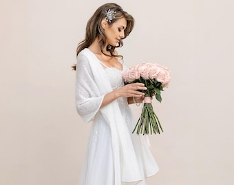May include: A bride in a white wedding dress and a sequined shawl holds a bouquet of pink roses. She wears a decorative hairpiece. The dress has a tulle skirt and a beaded bodice. The bouquet is tied with a pink ribbon.