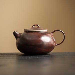 May include: A white ceramic mug with a black handle and the text "But First, Coffee" in a bold, black font. The mug is set against a neutral background, highlighting its simple design.