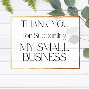 K&ouml;nnte beinhalten: Ein wei&szlig;es rechteckiges Schild mit goldenem Rand zeigt den schwarzen Text "THANK YOU for Supporting MY SMALL BUSINESS". Gr&uuml;ne Bl&auml;tter und Farnwedel befinden sich im Hintergrund, vor einer wei&szlig;en Holzpaneeloberfl&auml;che.