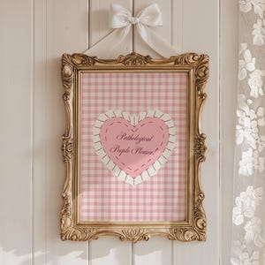 May include: A gold framed picture with a pink and white gingham background. A pink heart with a stitched border and the text "Pathological People Pleaser!" is in the center of the picture.
