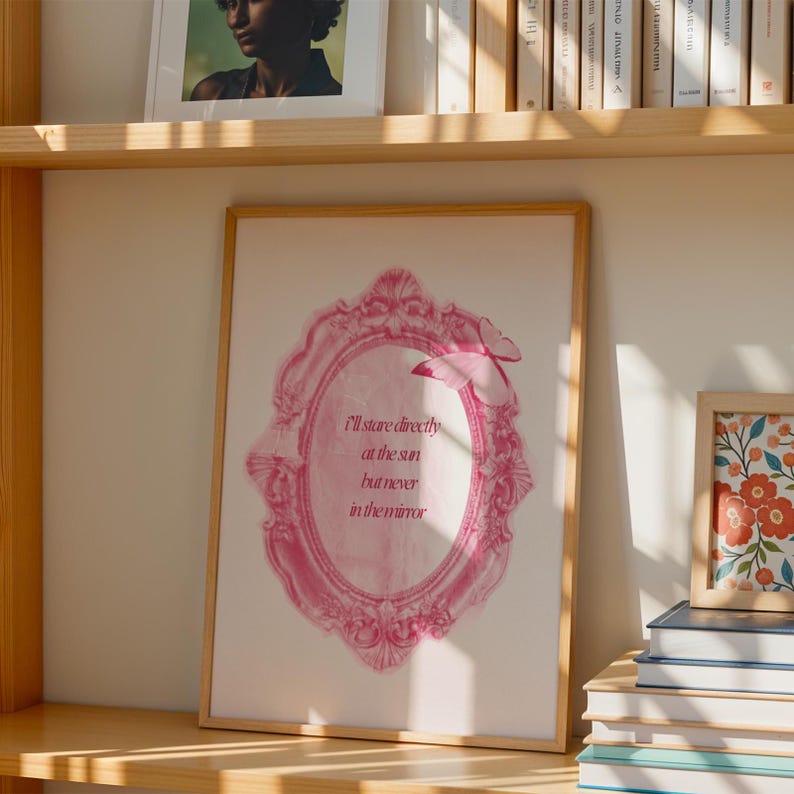 Pode incluir: Impress&atilde;o emoldurada rosa com uma cita&ccedil;&atilde;o que diz "Vou olhar diretamente para o sol, mas nunca para o espelho". A moldura &eacute; ornamentada e tem um design de borboleta.