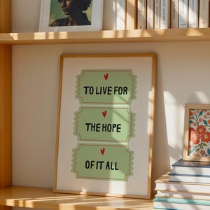 K&ouml;nnte beinhalten: Ein gerahmter Druck mit gr&uuml;nem Hintergrund und drei ticketf&ouml;rmigen Designs. Jedes Ticket hat ein rotes Herz und einen Text, der "To Live For", "The Hope" und "Of It All" lautet.