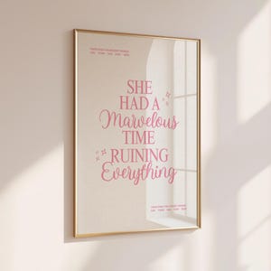 Pode incluir: Uma impressão emoldurada com uma borda dourada. A impressão tem um fundo bege com texto rosa que diz "SHE HAD A Marvelous TIME RUINING Everything". A impressão está pendurada em uma parede bege clara.