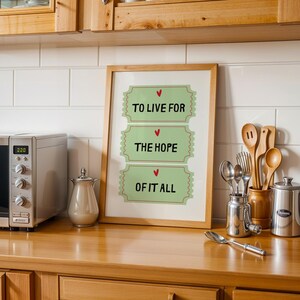 K&ouml;nnte beinhalten: Ein gerahmter Druck mit gr&uuml;nem Hintergrund und drei ticketf&ouml;rmigen Designs. Jedes Ticket hat ein rotes Herz und den Text "To Live For", "The Hope" und "Of It All".
