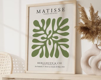 May include: A framed art print featuring a green abstract design with the text "MATISSE PAPIERS DÉCOUPÉS" and "BERGGRUEN & CIE". The print is displayed on a light wood cabinet with a woven chair and decorative vases.