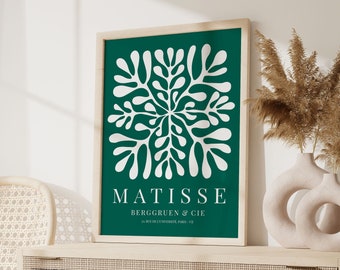 May include: A framed art print featuring a white floral design on a dark green background. The print includes the name "MATISSE" and other text. The artwork is displayed on a light wood cabinet with decorative vases and a woven chair.