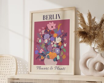 May include: A framed print with a pink background featuring a bouquet of colourful flowers in a pink vase. The print has the text "BERLIN" and "Flowers & Plants" in a dark blue font.