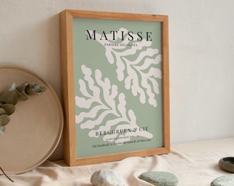 May include: A framed print of a Matisse artwork titled "Papiers Decoupés" with a green background and white abstract shapes. The print is framed in a light wood frame and includes the text "Berggruen & Cie" and the dates "Du Vendredi 22. Février au Samedi 24 Mars 1973".