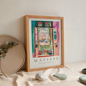 Peut inclure: Une impression encadrée d'une peinture d'Henri Matisse intitulée "La Fenêtre ouverte - Paris, France - 1905". La peinture représente une vue colorée depuis une fenêtre avec un balcon et des bateaux au loin.