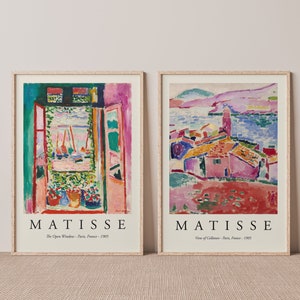 Puede incluir: Dos impresiones de arte enmarcadas de pinturas de Henri Matisse. La primera impresión muestra una vista colorida de una habitación con una ventana abierta y una vista de barcos en el agua. La segunda impresión muestra una vista colorida de un pueblo con casas y una iglesia.