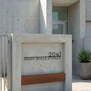 May include: Contemporary concrete house exterior featuring a metal gate and a sign displaying "2041 MARY MILLS STREET". A wooden bench is beneath the sign. Two large potted plants are positioned to the right of the entrance.