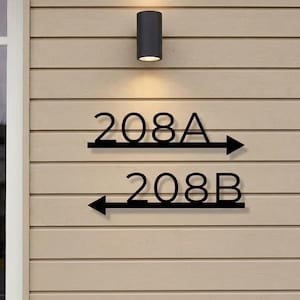 May include: Black metal address sign with the numbers 208A and 208B. The number 208A has an arrow pointing right, and 208B has an arrow pointing left. The sign is mounted on a light brown, horizontal wood-paneled wall.