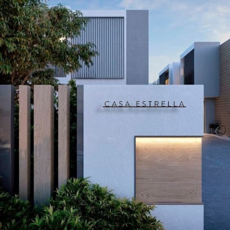 May include: Exterior view of a modern building with a sign that reads "CASA ESTRELLA". The building features a light-colored facade, wooden accents, and a decorative wooden panel with warm lighting. A bicycle is parked nearby.