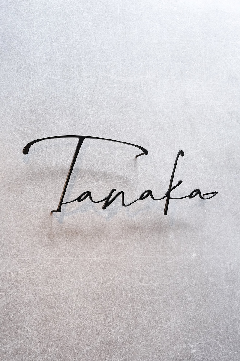 May include: A black metal sign with the word "Tanaka" written in a cursive script.