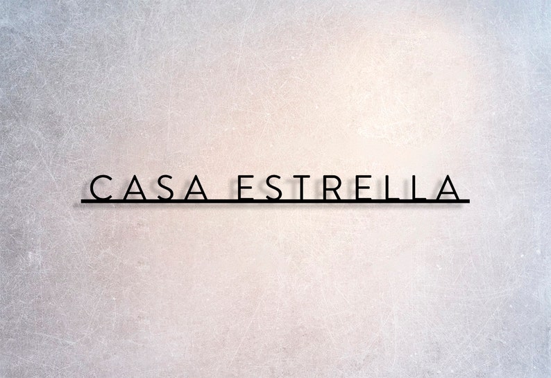 May include: The image features the text "CASA ESTRELLA" in a sleek, minimalist black font. The text is centered and positioned above a thin, horizontal black line. The background has a textured, light gray and white gradient.