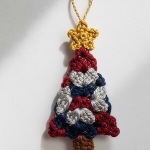 May include: A handmade crochet Christmas tree ornament. The tree is made of red, white, and blue yarn, with a gold star on top and a brown trunk. A gold string is attached for hanging.