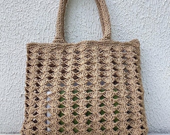 May include: A tan crochet tote bag with two handles. The bag has an open weave design, allowing a glimpse of the contents inside. The bag is made of a natural fiber material and is suitable for carrying various items.