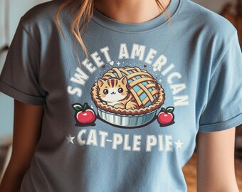 May include: A light blue t-shirt with a cartoon cat inside a pie. The text on the shirt reads "Sweet American Cat-Ple Pie".