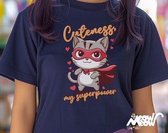 Könnte beinhalten: Ein marineblaues T-Shirt mit einer Comic-Katze, die eine rote Maske und einen Umhang trägt. Der Text "Cuteness, my superpower" ist auf das Shirt gedruckt.