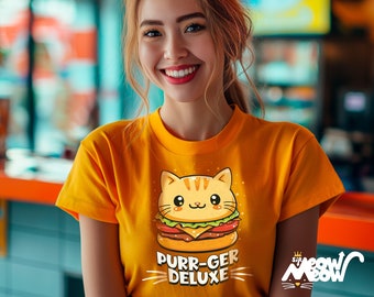 Puede incluir: Una mujer con una camiseta amarilla con un gato de dibujos animados comiendo una hamburguesa. La camiseta dice "Purr-ger Deluxe" y tiene una pequeña corona con las palabras "Sir Meow Meow" en la esquina inferior derecha.