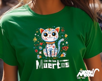 May include: Green t-shirt featuring a colorful cat design with floral and heart accents, and the text "Dia de los Muertos". The cat has a sugar skull design. The shirt also has the text "Sip Meow Meow".