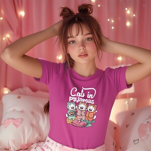 May include: A pink t-shirt with a white graphic of three cats wearing pajamas and the text "Cats in pajamas".