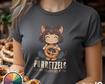 Könnte beinhalten: Ein dunkelgraues T-Shirt mit einer Cartoon-Illustration einer Katze, die einen Brezel hält. Der Text "Purretzels" ist auf dem Shirt aufgedruckt, zusammen mit dem Satz "Cats and pretzels fuel my day."
