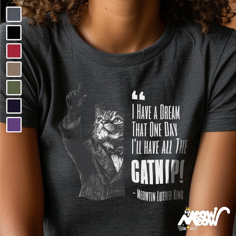May include: A dark gray t-shirt with a black and white illustration of a cat wearing a tuxedo and holding a finger up. The text on the shirt reads "I have a dream that one day I'll have all the catnip! - Meowtin Luther King"