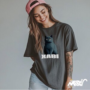 May include: A charcoal gray t-shirt with a black cat illustration and the text "XABI" in white. The cat has yellow eyes and is sitting on a gray background.