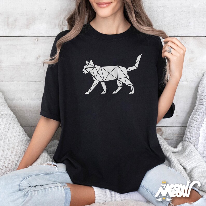 May include: Black t-shirt featuring a geometric cat design in white. The cat illustration is made up of interconnected triangles and lines, creating a modern, minimalist aesthetic. The shirt has a classic crew neck and short sleeves.