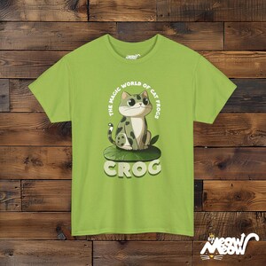 May include: A light green t-shirt with a cartoon cat sitting on a lily pad. The cat is green, white, and black. The text on the shirt reads "The Magic World of Cat Frogs Crog".