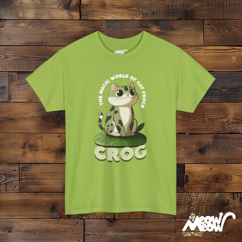 May include: A light green t-shirt with a cartoon cat sitting on a lily pad. The cat is green, white, and black. The text on the shirt reads "The Magic World of Cat Frogs Crog".