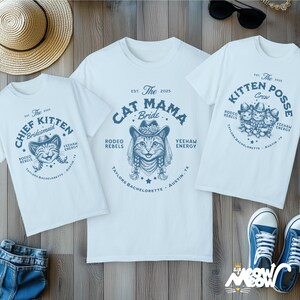 May include: Three white t-shirts with blue graphics and text. One shirt says "Cat Mama Bride" with a cat wearing a cowboy hat. Another says "Chief Kitten Bridesmaid" with a cat face. The third says "Kitten Posse Crew".
