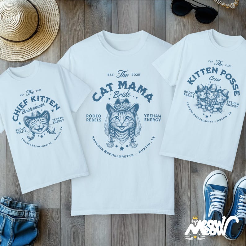 May include: Three white t-shirts with blue graphics and text. One shirt says "Cat Mama Bride" with a cat wearing a cowboy hat. Another says "Chief Kitten Bridesmaid" with a cat face. The third says "Kitten Posse Crew".