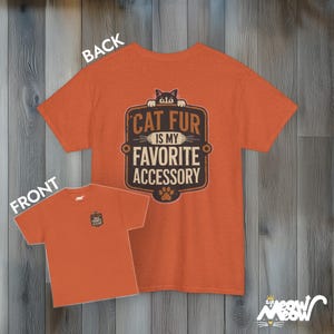 May include: Orange t-shirt with a brown and white graphic that says "Cat Fur is my Favorite Accessory". A black cat is peeking over the top of the graphic. The back of the shirt is plain orange.
