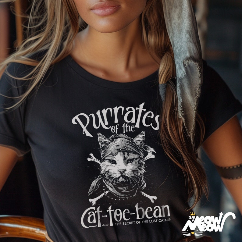May include: Black t-shirt with a white graphic of a cat wearing a pirate bandana and holding crossed bones. The text reads "Purrates of the Cat-toe-bean" and "The Secret of the Lost Catnip".