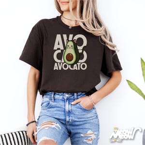 May include: A brown t-shirt with a graphic of a cat inside an avocado. The text "AVO CATO AVOCATO" is printed on the shirt.