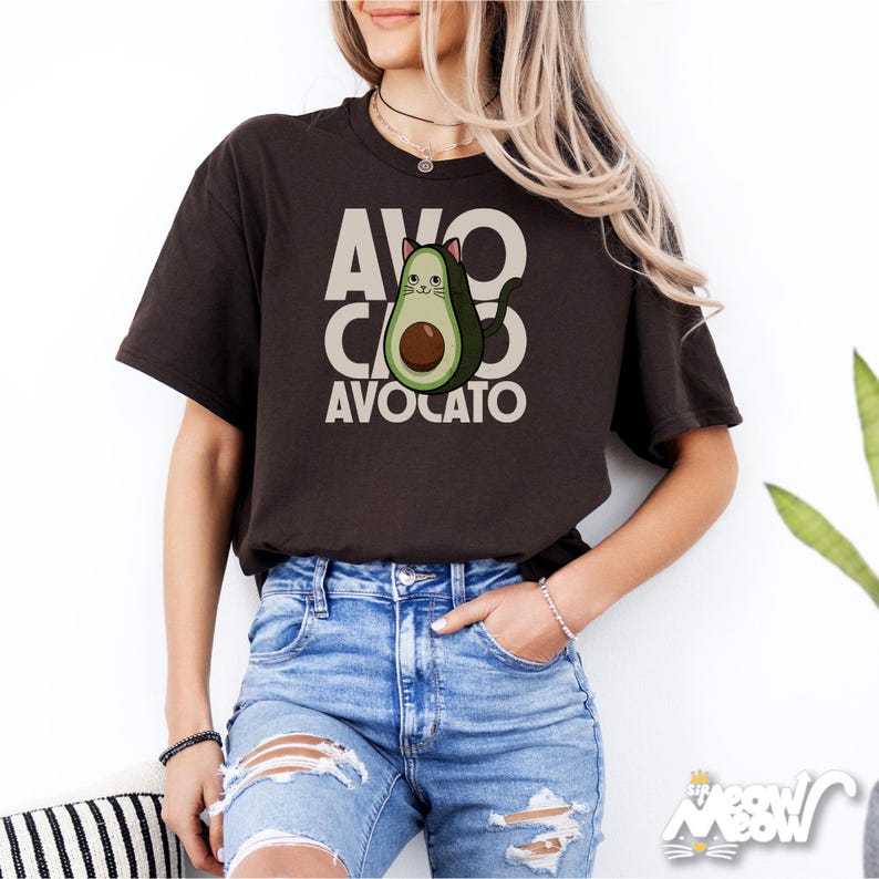 May include: A brown t-shirt with a graphic of a cat inside an avocado. The text "AVO CATO AVOCATO" is printed on the shirt.