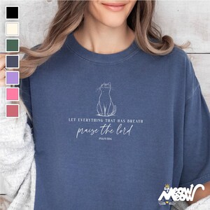 Op de afbeelding: Een blauw t-shirt met een witte omtrek van een kat en de tekst "Laat alles wat adem heeft de Heer prijzen Psalm 150:6".