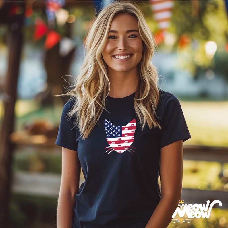 May include: A woman wearing a navy blue t-shirt with a cat silhouette design. The cat is made up of the American flag with paw prints instead of stars.
