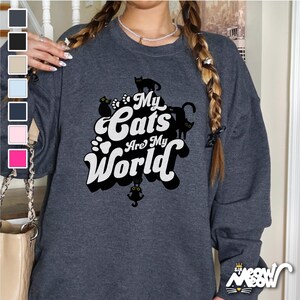 Puede incluir: Una sudadera gris oscuro con un estampado gráfico blanco que dice "My Cats Are My World" con siluetas de gatos negros.