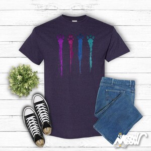 May include: A dark purple t-shirt featuring a graphic of four colourful paw prints dripping paint. The paw prints are in shades of purple, pink, blue, and green.