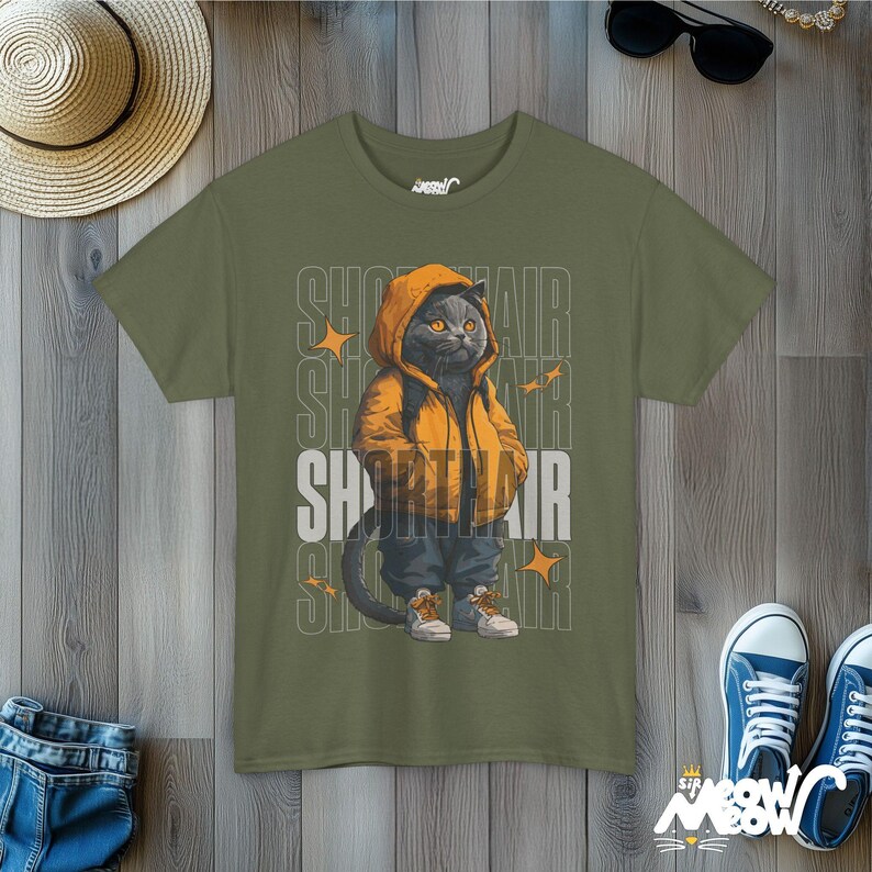 Humanized British Shorthair Cat standing up wearing a yellow hoodie and white and gray sneakers. Behind the cat is a stack of the word "Shorthair". The design appears on a woman wearing a army green tee.