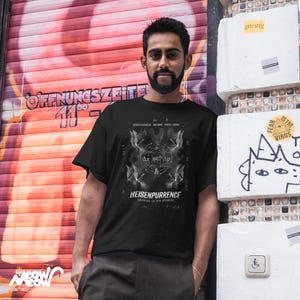 May include: Black t-shirt with a graphic design featuring the text "HEISENPURRENCE" and mathematical symbols. The shirt also includes the text "KNOWING IS NOT KNOWING". The design is in white against the black fabric.