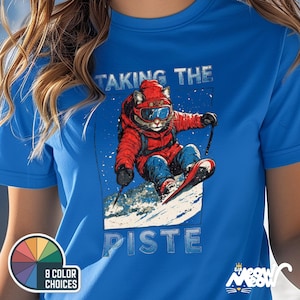 K&ouml;nnte beinhalten: Ein blaues T-Shirt mit einem Aufdruck eines katzenartigen Wesens, das Ski f&auml;hrt. Der Text "Taking the Piste" ist auf dem Shirt aufgedruckt.