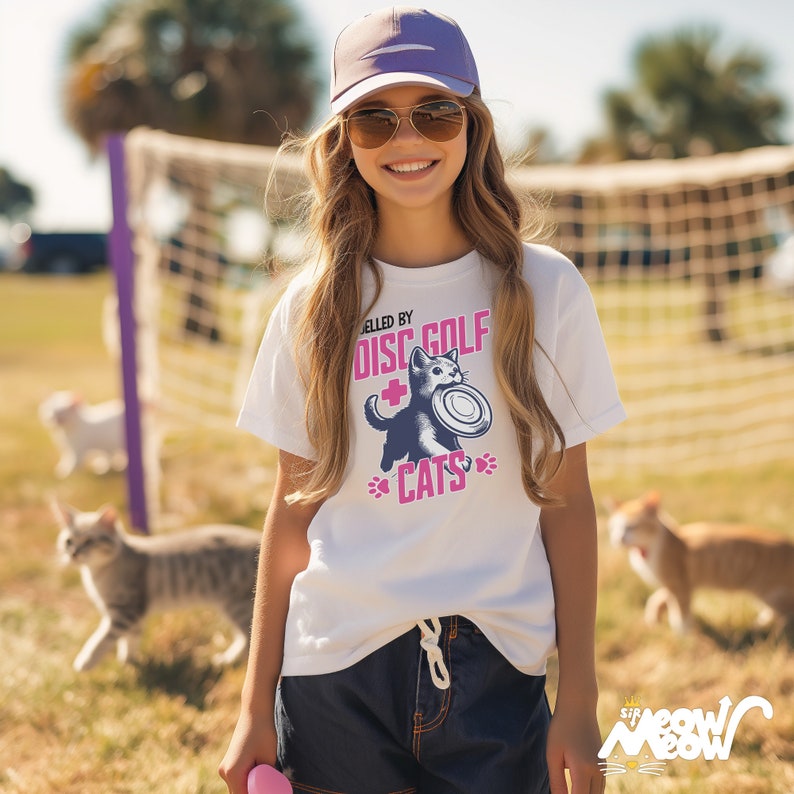 May include: White t-shirt with a black cat graphic holding a frisbee. The text "Obsessed by Disc Golf + Cats" is printed on the shirt in pink.
