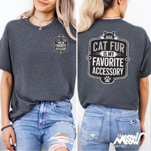 May include: A dark gray t-shirt with a black and white graphic on the front that says "Cat fur is my favorite accessory" and a larger graphic on the back that says "Cat fur is my favorite accessory" with a paw print below it.