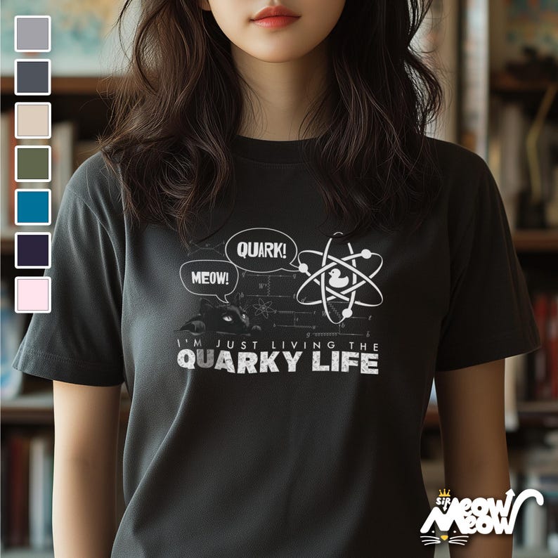 May include: A dark gray t-shirt with a white graphic of a cartoon duck in an atom. The text on the shirt reads "I'm just living the quirky life" with the words "quark!" and "meow!" in speech bubbles.