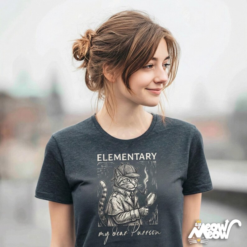 May include: Dark gray t-shirt featuring a detective cat illustration with the text "ELEMENTARY my dear Purrson". The cat is wearing a hat and trench coat, holding a magnifying glass and smoking a pipe. The shirt has a crew neck.